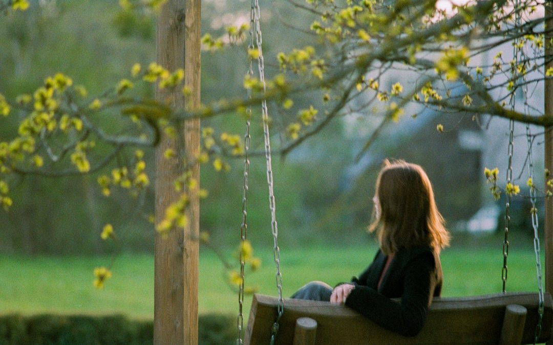 Young woman sitting on a swing in a sunny garden.